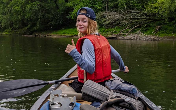 a student in a canoe gives a thumbs up on a canoeing trip with outward bound